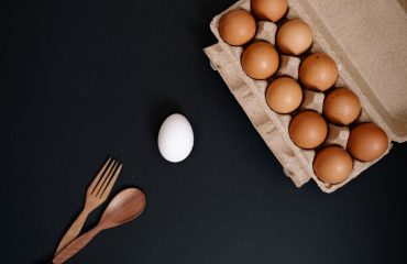 Brown eggs in carton with single white egg on dark background. Minimalist food concept.